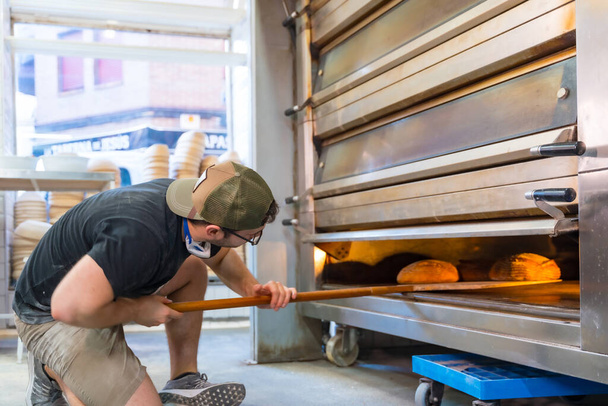 Baker of bakery in the workshop workshop of artisan bakery baking loaves in the oven - Foto, Bild