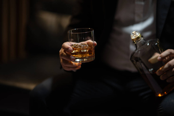 Empresario sentado sosteniendo un vaso de whisky beber whisky en el almacén de licores - Foto, imagen