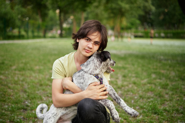 Εξωτερικό πορτρέτο του αγοριού με τον υιοθετημένο σκύλο του. Φιλία των εφήβων με κατοικίδιο ζώο, αγόρι περπάτημα στο θερινό λιβάδι, γραφικό ηλιοβασίλεμα τοπία φόντο. Υψηλής ποιότητας φωτογραφία - Φωτογραφία, εικόνα