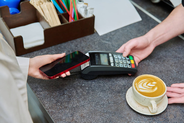 Close-up of a customers hand with a smartphone paying for a cup of coffee in a cafe, contactless using the terminal, mobile payment - Foto, immagini