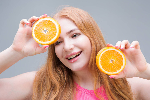 灰色の背景にオレンジのジューシーな半分を持つ幸せな若い女性。健康的な食事の概念。国会. - 写真・画像