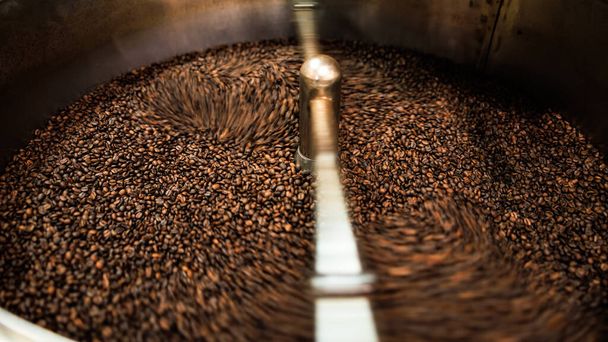 fresh coffee beans roasted spinning cover professional machine close up to soft focus  slow shutter speed because want to make motion blur of coffee beans detail concept, at factory chiang rai Thailand, angle view shot. - Valokuva, kuva
