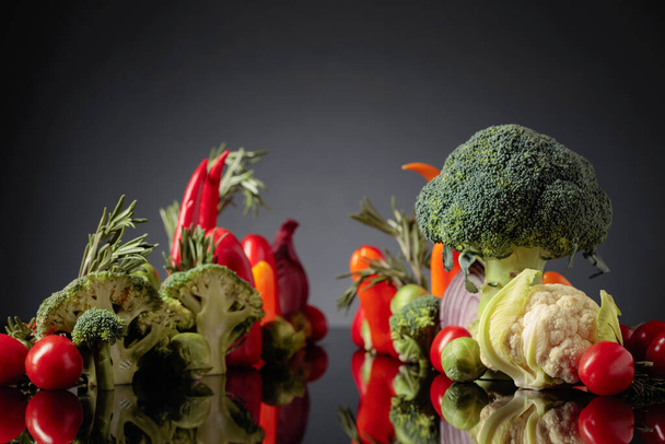 Различные сырые овощи на черном отражающем фоне. Концептуальный образ на тему вегетарианства.  - Фото, изображение