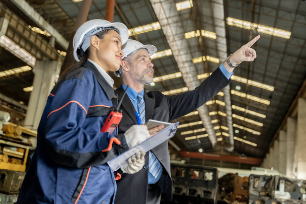 A business man inspects the work of an on-site worker at an old factory for rehearsing train engines.	 - Foto, immagini