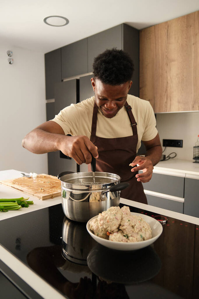 Young african man preparing boiled chicken mince with vegetables recipe in a kitchen. - Photo, Image