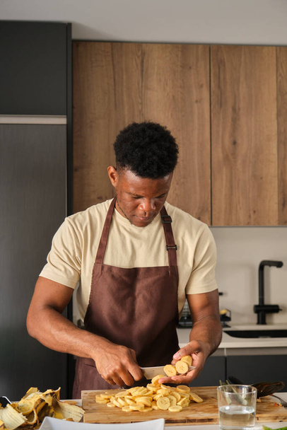 Giovane uomo africano tagliare banane in una cucina. - Foto, immagini