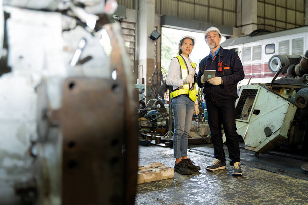 Un hombre de negocios inspecciona el trabajo de un trabajador in situ en una antigua fábrica para ensayar motores de tren. - Foto, imagen