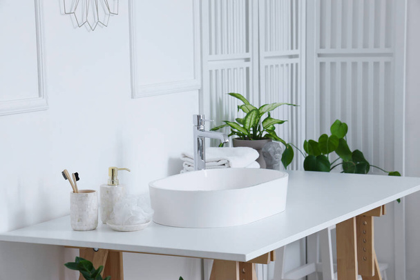 Interieur van lichte badkamer met witte wastafel, bad accessoires en kamerplanten - Foto, afbeelding