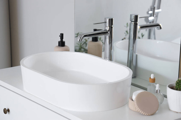 White sink and bath accessories on chest of drawers in light bathroom, closeup - Photo, Image