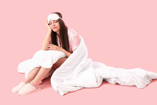 Mujer joven soñolienta con manta suave sentada sobre fondo rosa - Foto, Imagen
