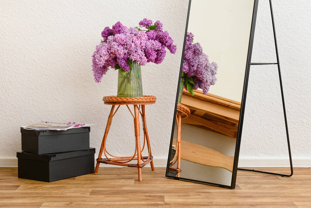 Ваза з красивими бузковими квітами на столі, дзеркало і коробки в інтер'єрі світлої вітальні - Фото, зображення