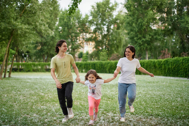 Lächelnde Familie läuft gemeinsam über Sommerfeld. Mutter Tochter Sohn, Hände zusammen Hochwertiges Foto - Foto, Bild