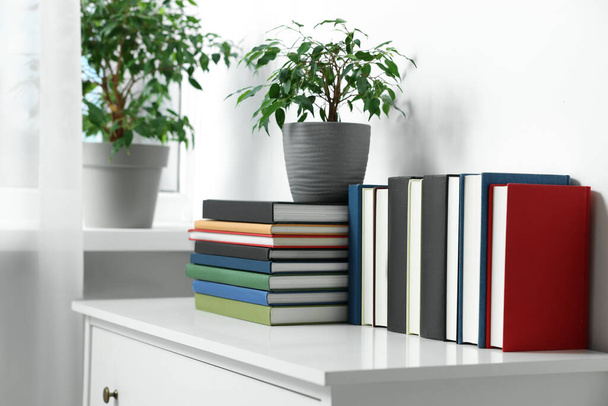 Many different books and potted plants on white cabinet indoors - Foto, immagini