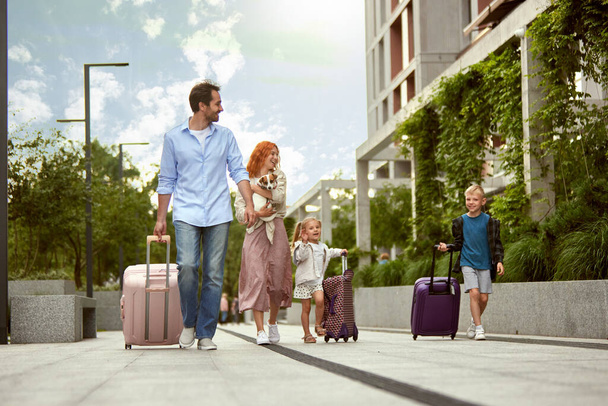 Young happy family, man and woman, parents going on vacation with little boy, girl and dog. Family trip. Warm summer day. Concept of family, childhood and parenthood, travelling, vacation, ad - Фото, изображение