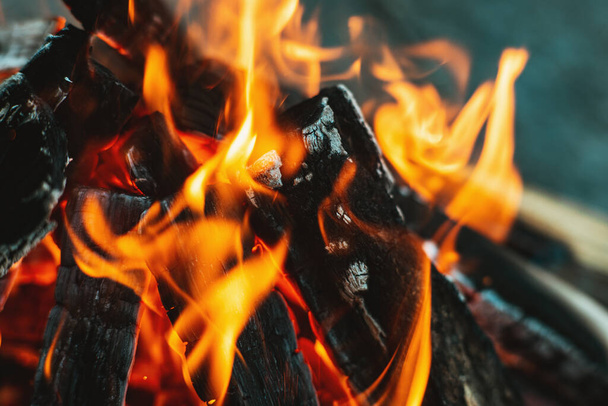 Una brillante llama de fuego sobre una fogata. La madera apilada en una pirámide está ardiendo. La llama del fuego de cerca. El humo blanco se eleva sobre el fuego. Fogata de barbacoa. Concepto turístico - Foto, Imagen