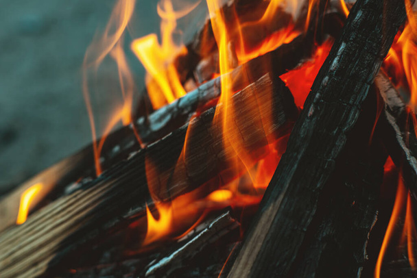 Płomień ognia nad ogniskiem. Drewniane drewno ułożone w piramidzie płonie. Płomień ognia z bliska. Nad ogniem wznosi się biały dym. Ognisko z grilla. Pojęcie turystyczne - Zdjęcie, obraz