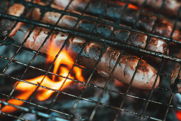 Les saucisses de lait sur un barbecue sont rôties sur un feu. Saucisses dans les flammes de l'incendie ourdoors. Délicieuses saucisses grillées. Vacances d'été. Barbecue - Photo, image