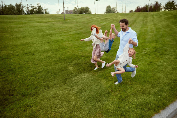 Young couple, man and woman going for a walk in park with their little children, boy and girl. Warm summer day walk. Concept of family, childhood and parenthood, fun, weekends, love, ad - Фото, зображення