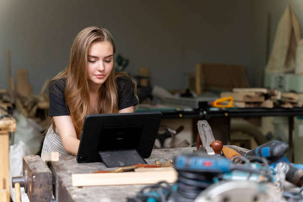 Portrait of a female carpenter looking at designs on a tablet for making her furniture in a furniture factory. with many tools and wood - Foto, Bild