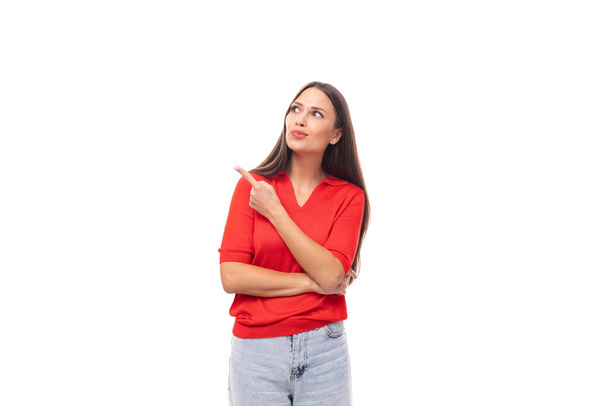 портрет милої молодої європейської брюнетки в червоній футболці активно жестикулює своїм індексним пальцем до стіни. - Фото, зображення