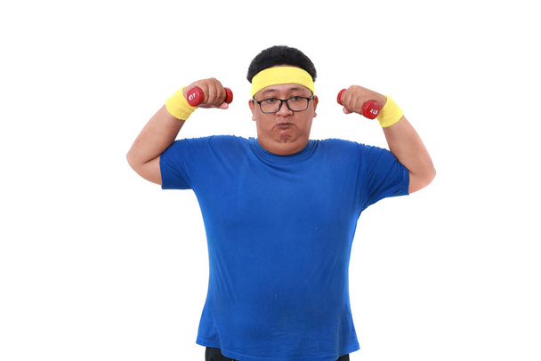 ダンベルを抱えながらスポーツウェア姿のアジア系太りすぎ男。白地に隔離された - 写真・画像