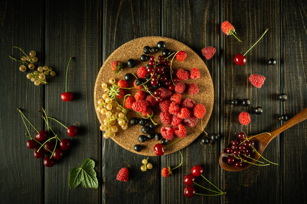 Lots of currants and raspberries and cherries on a dark kitchen table before preparing a berry drink. Fruit drink preparation concept. - Valokuva, kuva
