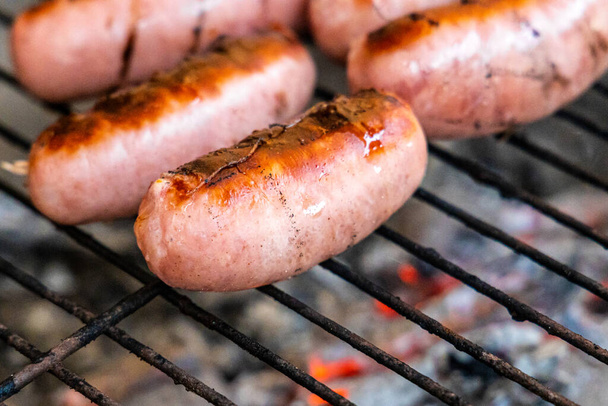 The Group of delicious pink sausages on a black metal grille fried for a picnic are in a fireplace in the forest - Фото, изображение