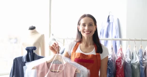 Glimlachende vrouw met kleren in plastic zakken in handen in wasserij 4k film. Stomerij van kleding concept - Video