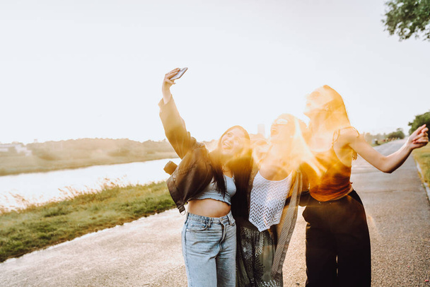 party young happy girls in nature. company young women, teenage girls, smiling, with hair wet from rain, having fun, taking selfies and dancing in nature by river, in rays of setting sun, glare lens - Fotó, kép