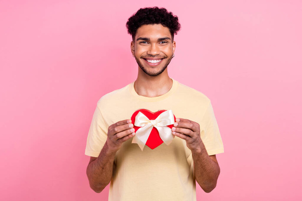 Portrait of positive cheerful man with afro hair earrings stubble holding present heart shape box isolated on pink color background. - Foto, afbeelding
