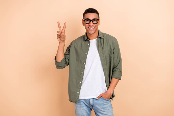 Portrait of cheerful attractive man toothy smile hand fingers demonstrate v-sign isolated on beige color background. - Foto, imagen