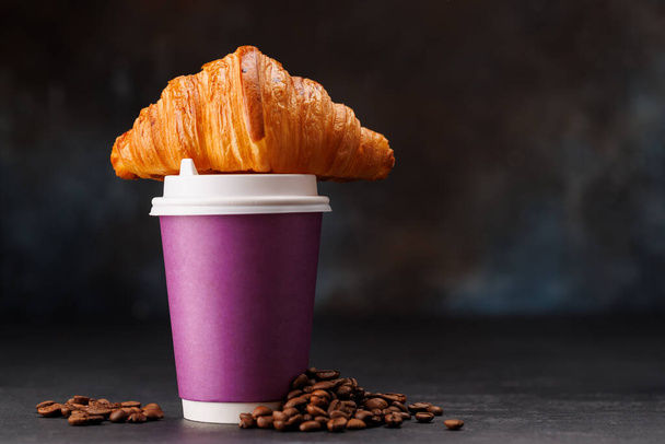 Aromatische koffie in een papieren beker gecombineerd met een schilferige croissant. met kopieerruimte - Foto, afbeelding