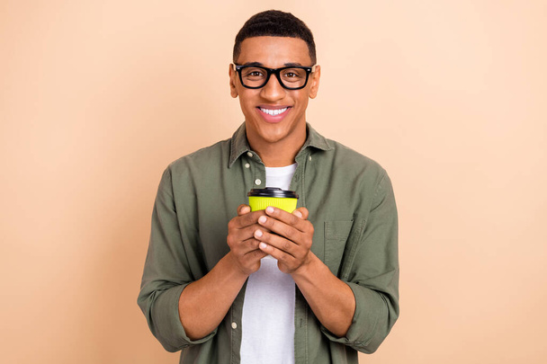 Portret zadowolonego człowieka dobry nastrój nosić stylowe okulary koszuli trzymać filiżankę aromatycznej kawy izolowane na beżowym tle koloru. - Zdjęcie, obraz