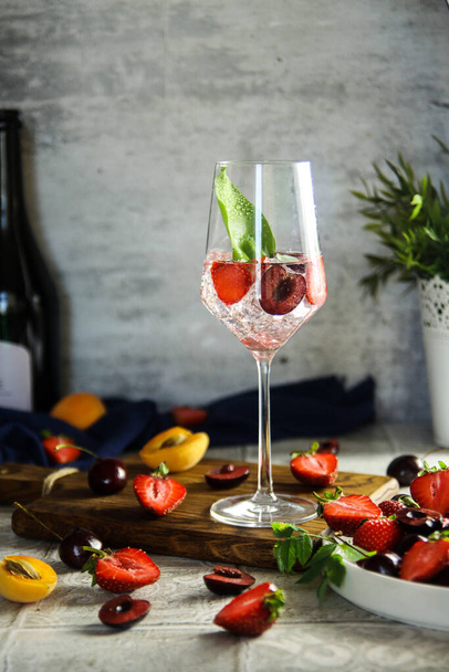 Sparlking wine with berries. Refreshing cooling sparkling summer drink with fresh strawberry, cherry and ice cubes. Prosecco champagne with ice cubes and berries - Photo, Image