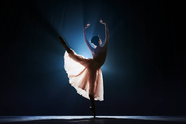 Şefkatli, zarif genç bir kadın silueti, sahne ışıklarıyla koyu mavi arka planda dans eden bir balerin gösterisi. Sanat konsepti, klasik bale, yaratıcılık, koreografi, güzellik, reklam - Fotoğraf, Görsel