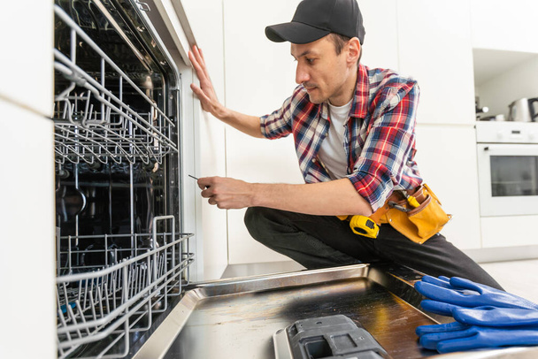 All instruments are included. Male technician standing near dishwasher with screwdriver in kitchen with instruments. High quality photo - Fotó, kép