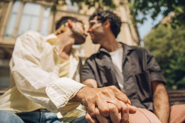 Concéntrate en las manos de una feliz pareja gay sentada en un banco de la ciudad.  - Foto, imagen