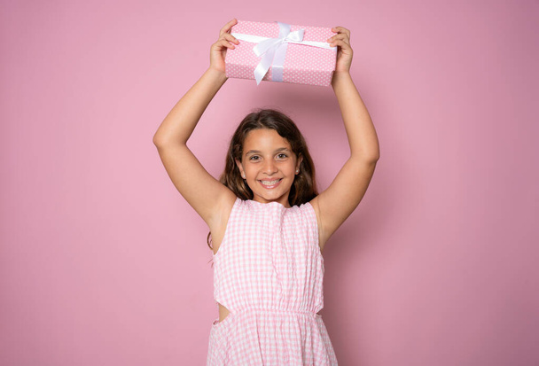 Picture of happy little girl child standing isolated over pink background. Looking camera holding gift box surprise. - Photo, image