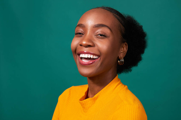 Mooie zwarte vrouw lachen in studio, teal achtergrond, mode lifestyle portret. Hoge kwaliteit foto - Foto, afbeelding