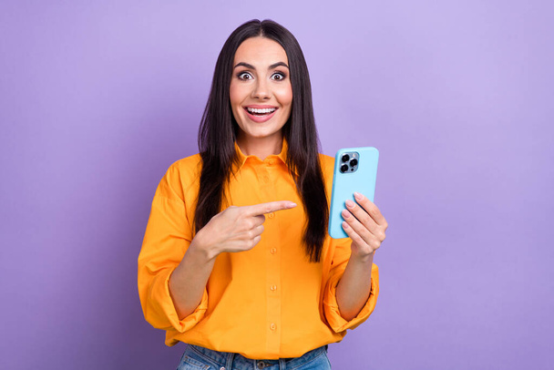 Portrait of overjoyed impressed woman with long hairstyle wear oversize shirt indicating at phone isolated on violet color background. - Valokuva, kuva