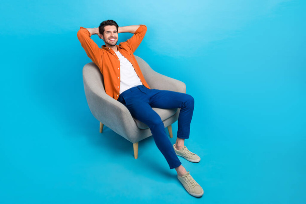 Full size portrait of cheerful peaceful young man sitting comfy soft chair hands behind head empty space isolated on blue color background. - Foto, Imagem