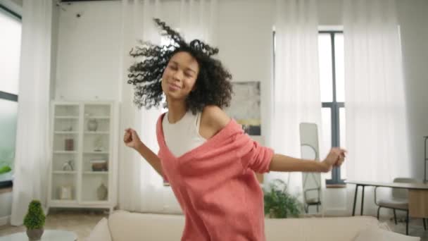 Geluk en plezier tijd concept video 4K. Slow motion mooie zwarte vrouw met afro haar hebben plezier glimlachen en dansen in stijlvolle eigentijdse design loft appartement tegen heldere ramen achtergrond - Video