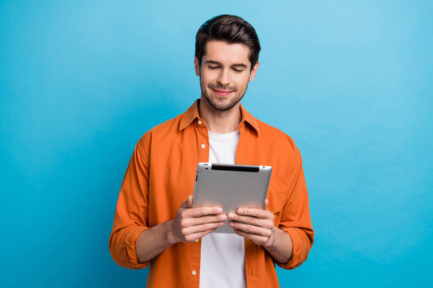 Photo of positive good mood guy wear orange shirt typing apple samsung gadget isolated blue color background. - Foto, Bild