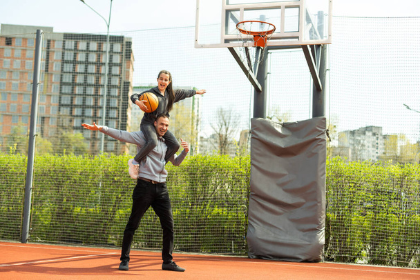 Babası, kızı omuzlarında taşıyarak basketbol topunu ağlara takmasına yardım ediyor. - Fotoğraf, Görsel