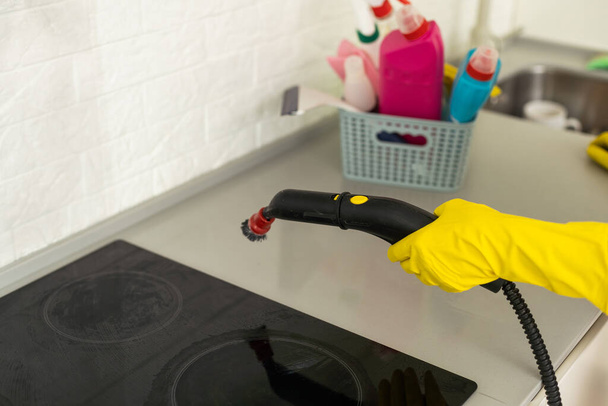Καλλιεργημένη φωτογραφία μιας γυναίκας με ομοιόμορφα φίλτρα καθαρισμού για απορροφητήρα κουζίνας με ατμοκαθαριστή, ενώ ο άνδρας συνάδελφός της εργάζεται στο παρασκήνιο. Η έννοια των υπηρεσιών καθαρισμού. Οικιακές εργασίες - Φωτογραφία, εικόνα