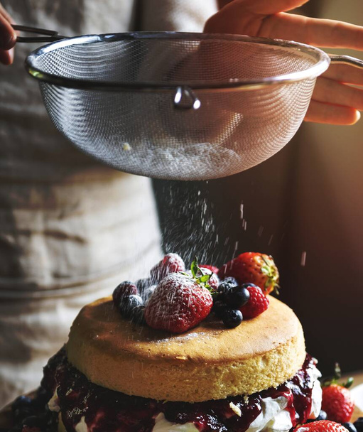 Woman sieving white powder over a layered cake - Foto, imagen