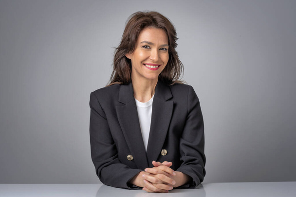 Portait of an attractive businesswoman wearing black blazer while sitting at isolated grey background. Copy space.  - Foto, Imagem