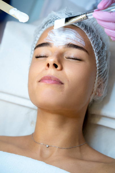 Unrecognizable cosmetologist applying mask to woman face in spa beauty salon. - Foto, Imagem