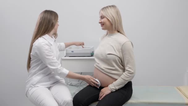 Az orvos felkészít egy terhes nőt a magzati szívverés ellenőrzésére magzati monitorozással. - Felvétel, videó
