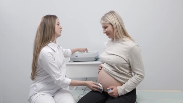 Az orvos felkészít egy terhes nőt a magzati szívverés ellenőrzésére magzati monitorozással. - Felvétel, videó